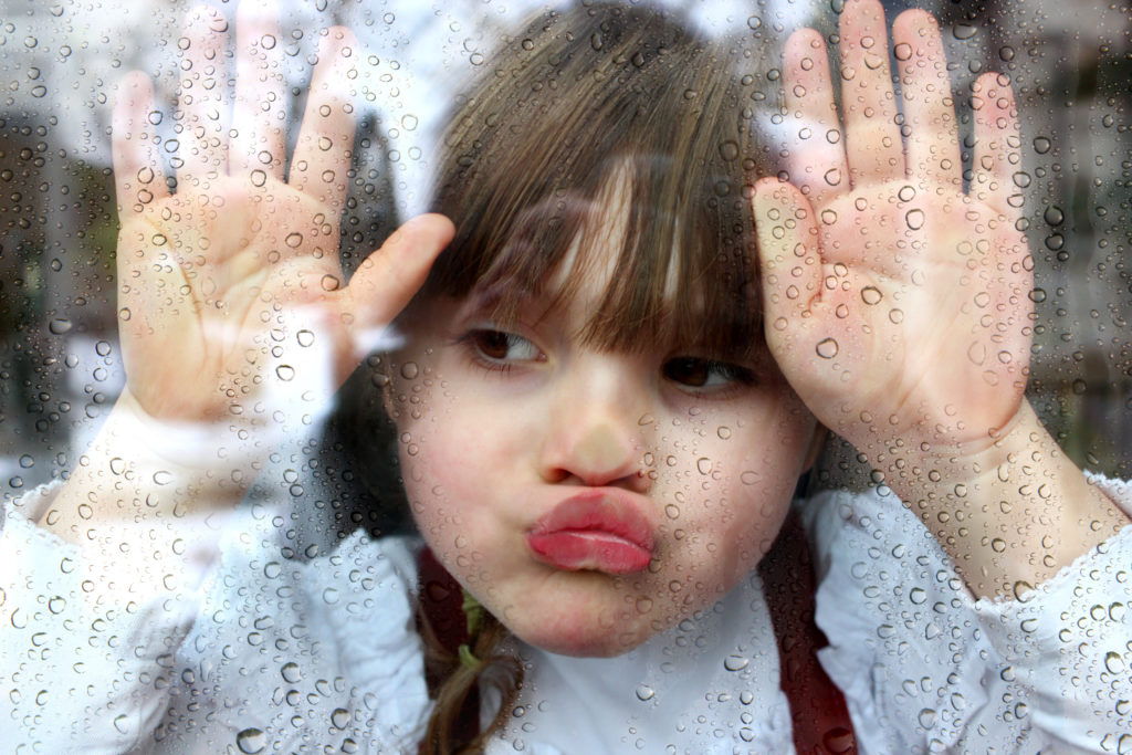 Kind schaut gelangweilt aus dem Fenster